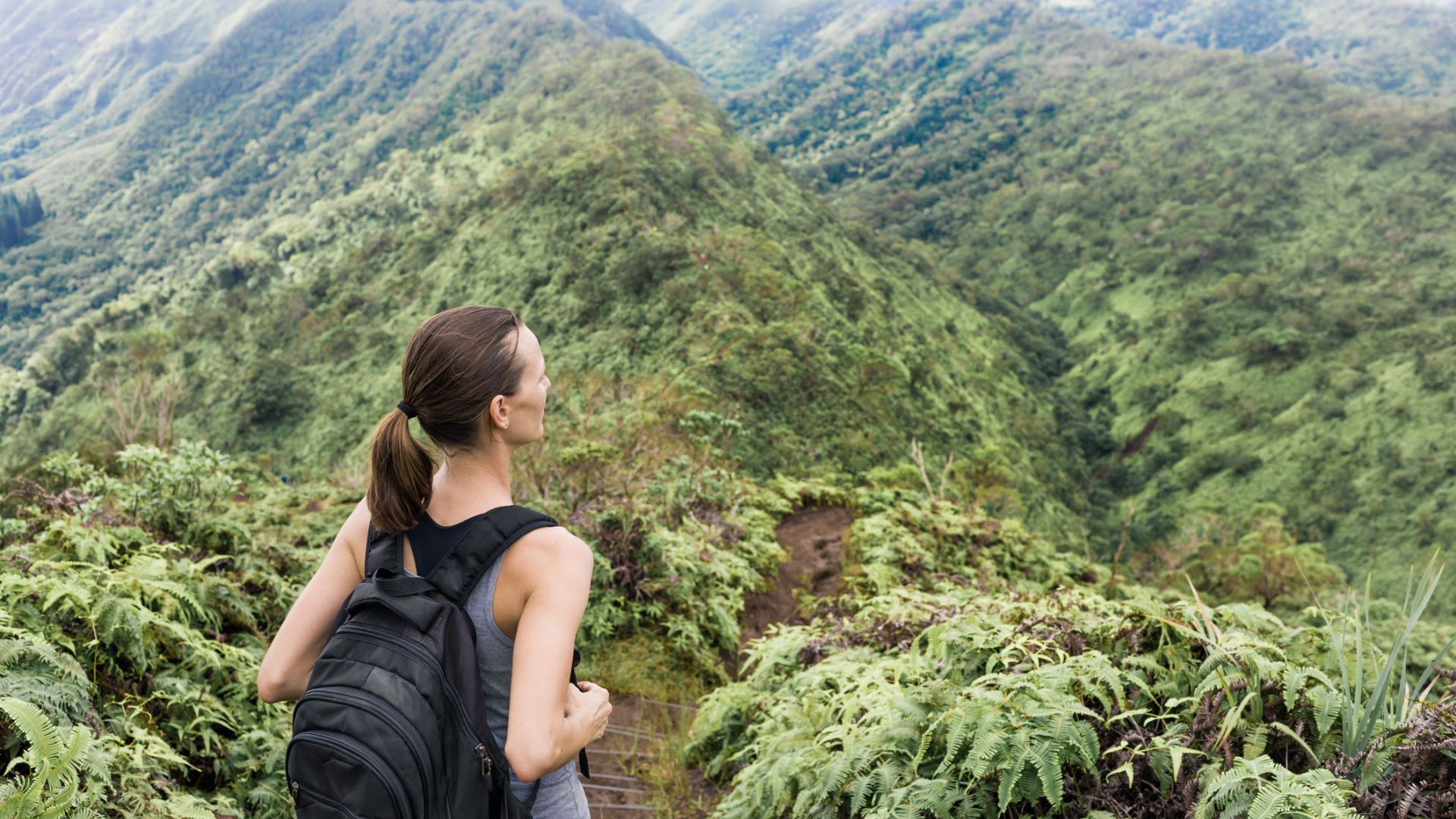 A female hiker with a backpack on standing on a lush hiking trail in Oahu