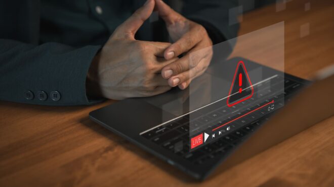 Hands at a laptop computer keyboard with a glowing warning error icon and livestream interface