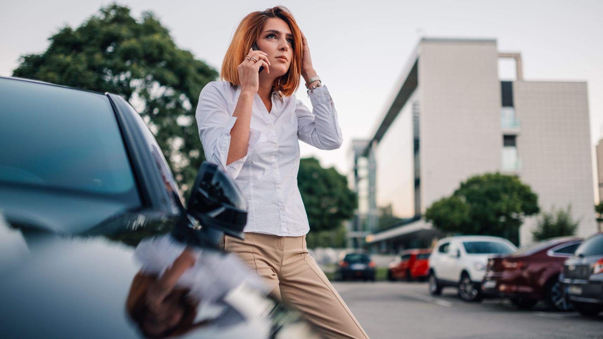 Woman upset outside her dark colored car on her cellphone in a parking lot
