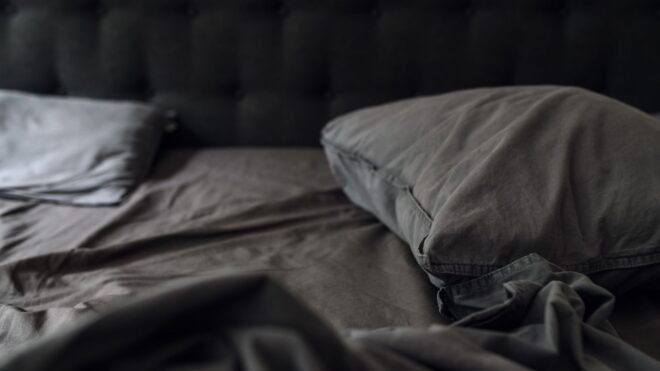 A creased gray bed with sheets and two pillows