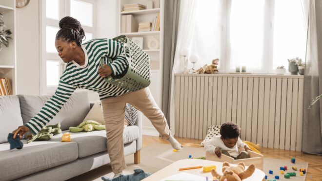 A mom trying to clean up her messy living room with a toddler playing nearby