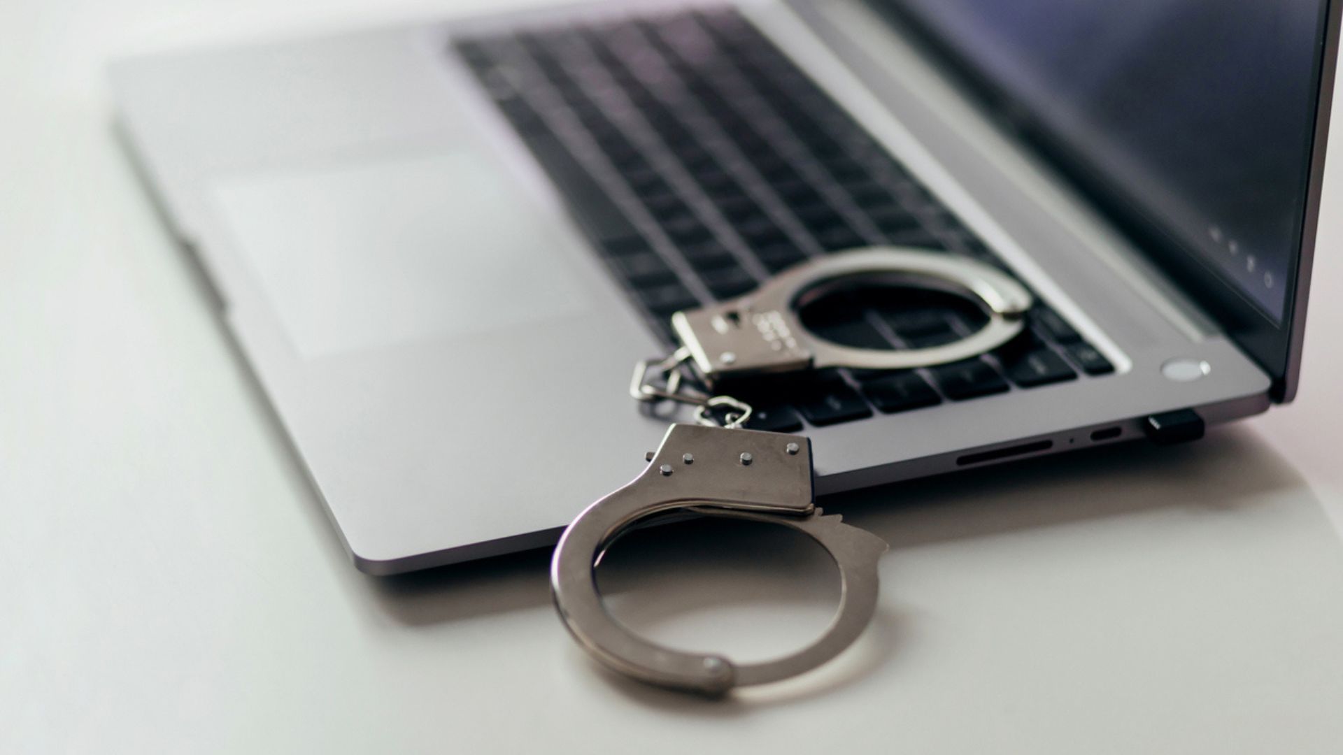A photo of an opened laptop with handcuffs nearby