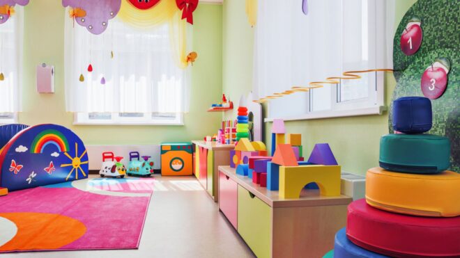 A stock image of a colorful kid's daycare room featuring a side table, toys, and a rug