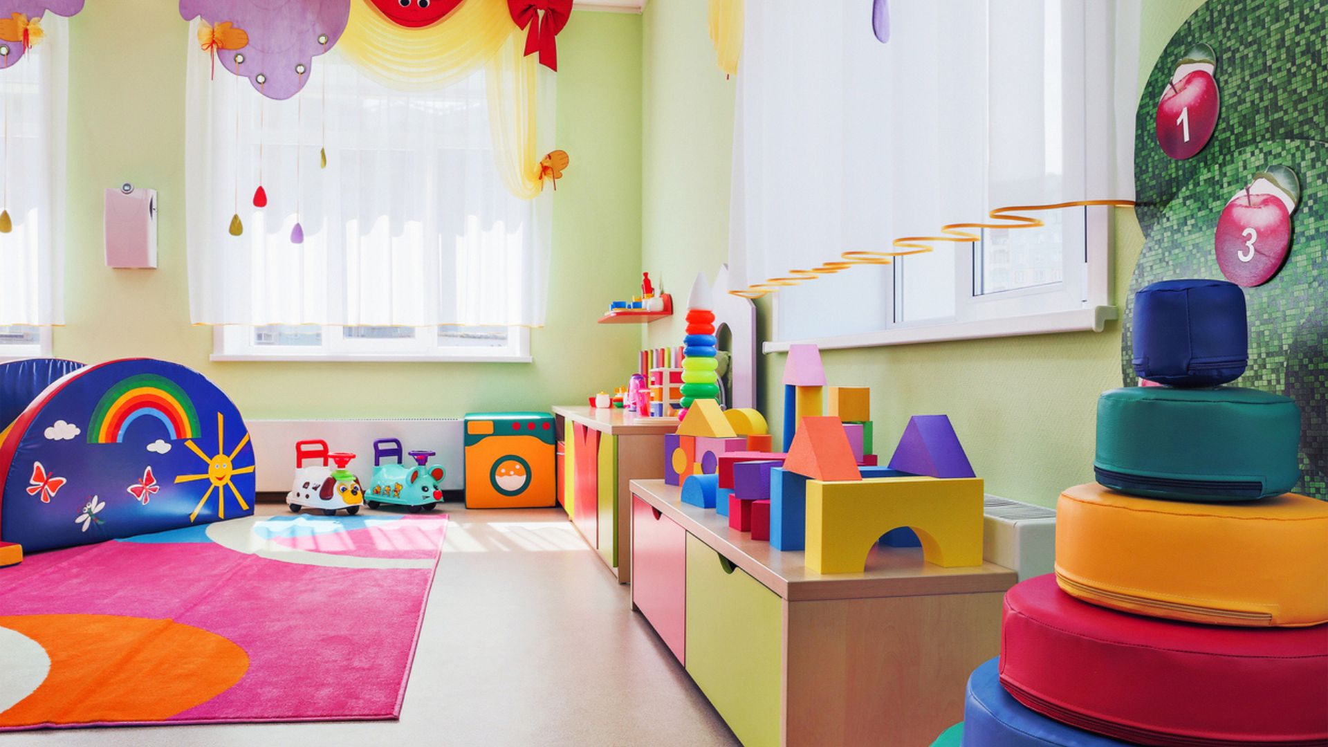 A stock image of a colorful kid's daycare room featuring a side table, toys, and a rug