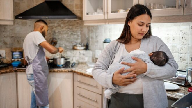 A woman holding her baby in the kitchen while the husband cooks at the stove