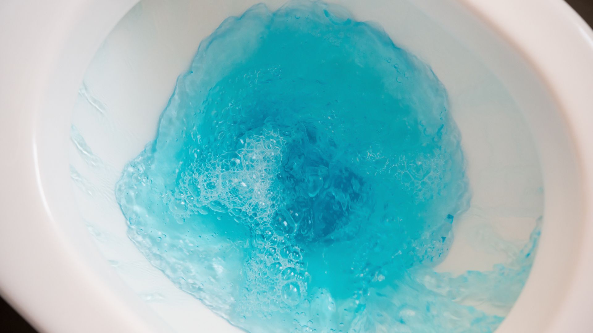 A close up of a toilet flushing with blue water inside