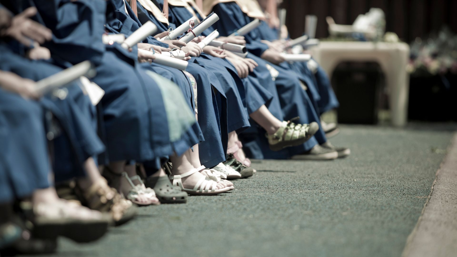 A kindergarten graduation photo featuring a lineup of shoes and kids holding their diplomas