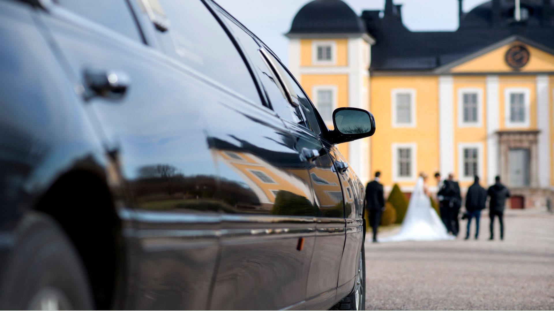 A limo arriving to a wedding venue with some of the wedding party outside a beautiful building