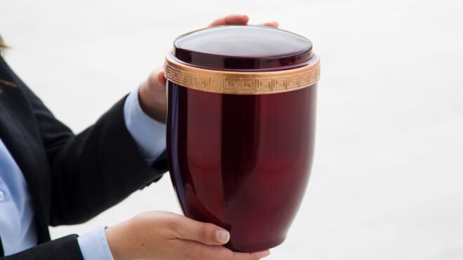A person holding a burgundy colored urn