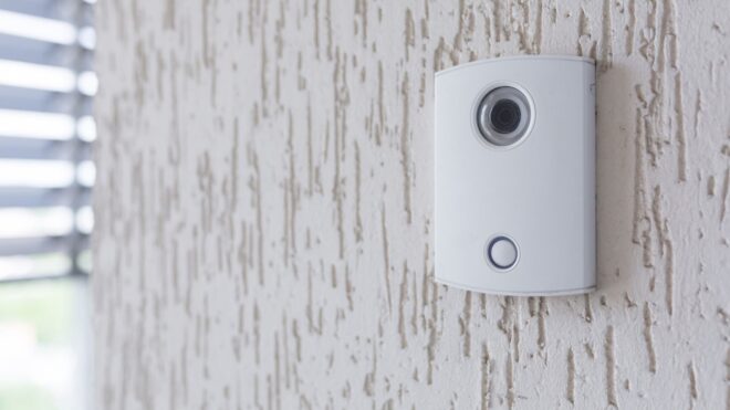 A white incoming electronic doorbell with a camera on the wall of the building
