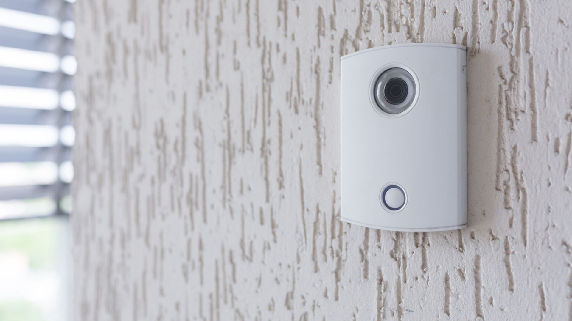 A white incoming electronic doorbell with a camera on the wall of the building