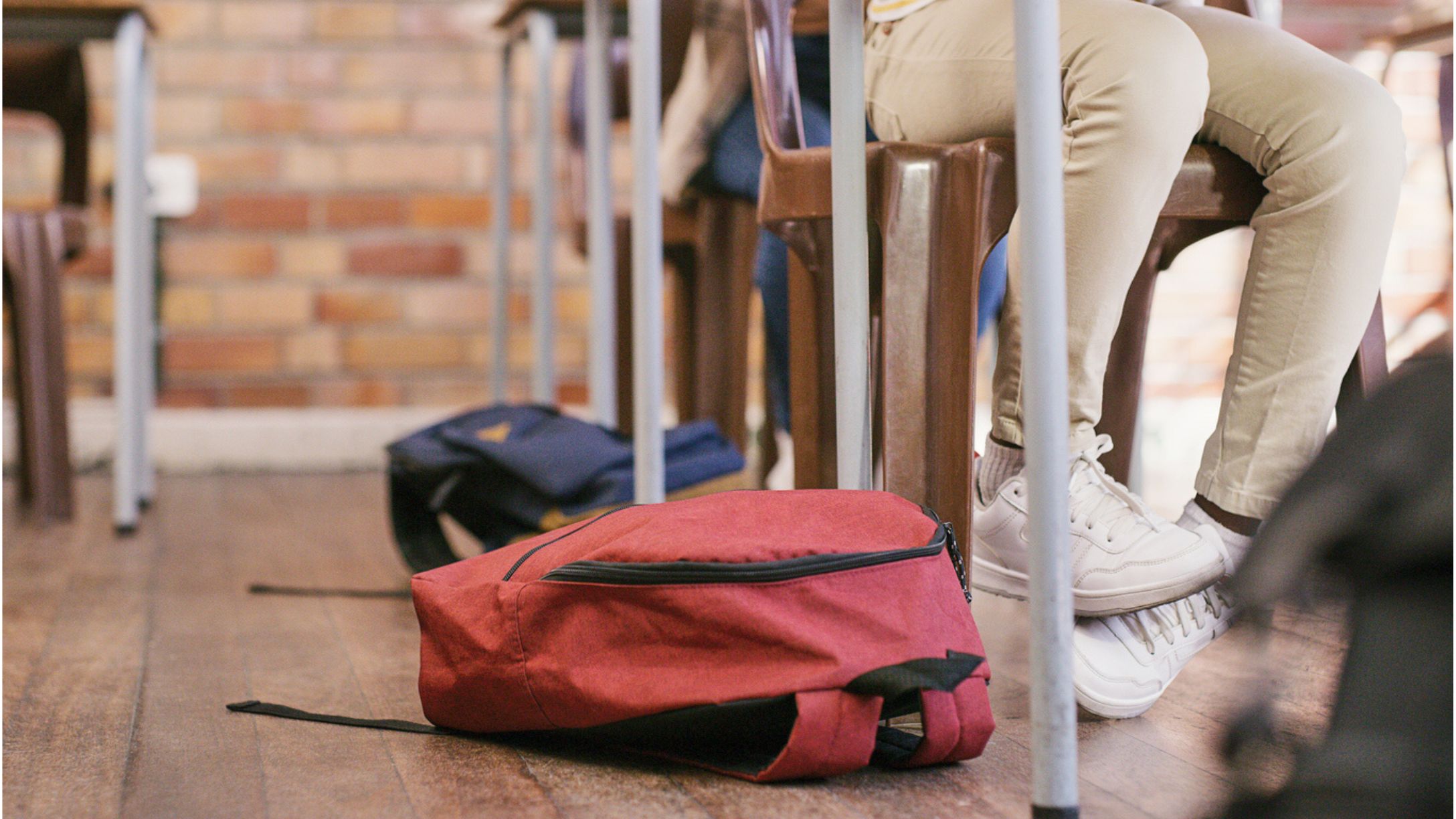 Legs of elementary school kids at their desks with a few backpacks on the ground