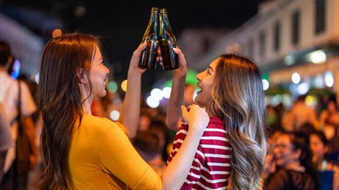 Two young adults cheersing their beers in a crowd of people