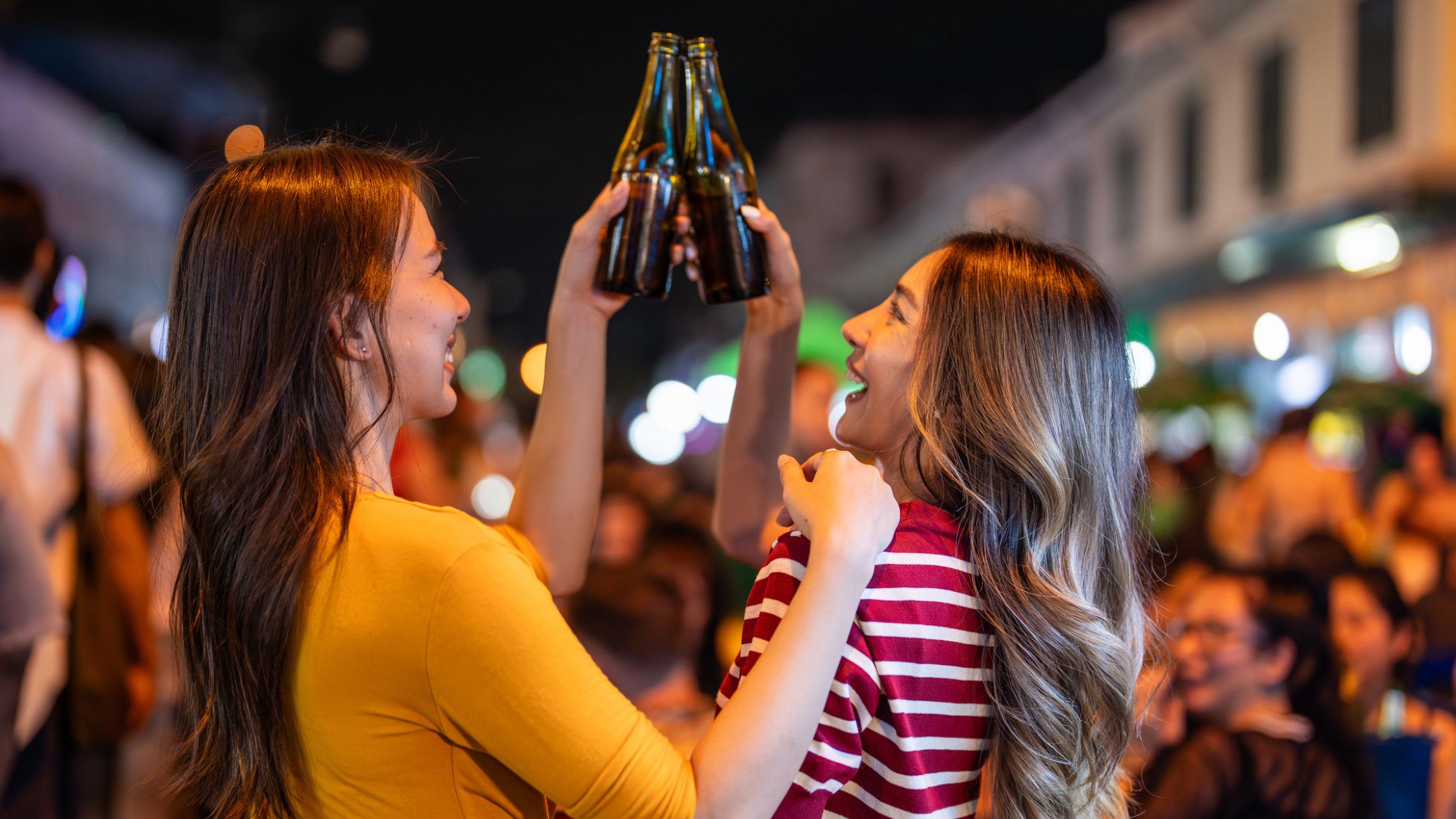 Two young adults cheersing their beers in a crowd of people