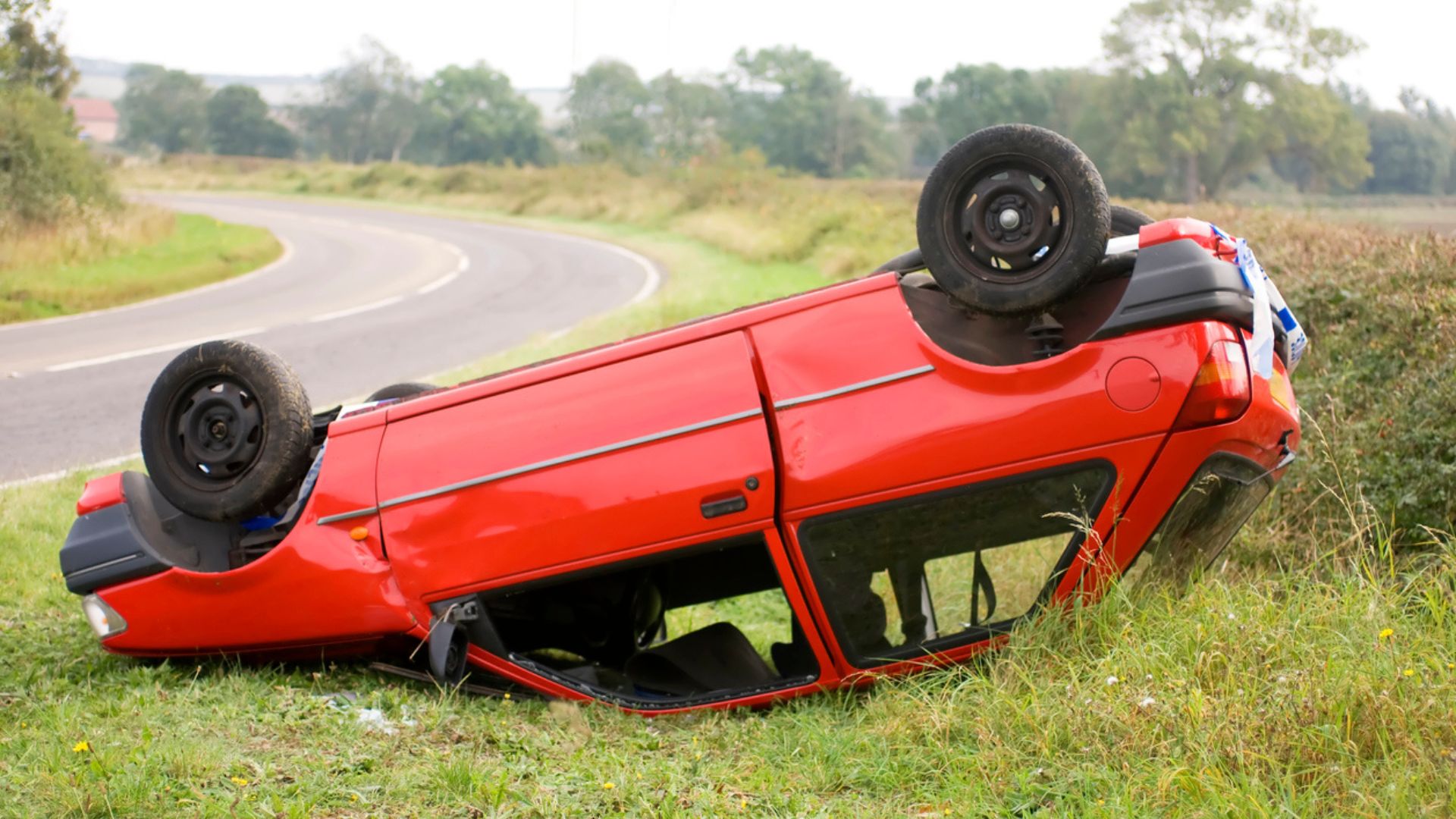 Upside down red car on the side of a grassy highway