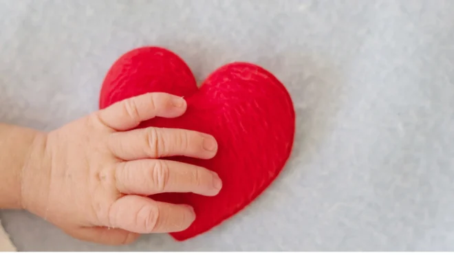 A baby's hand over top of a red felt heart