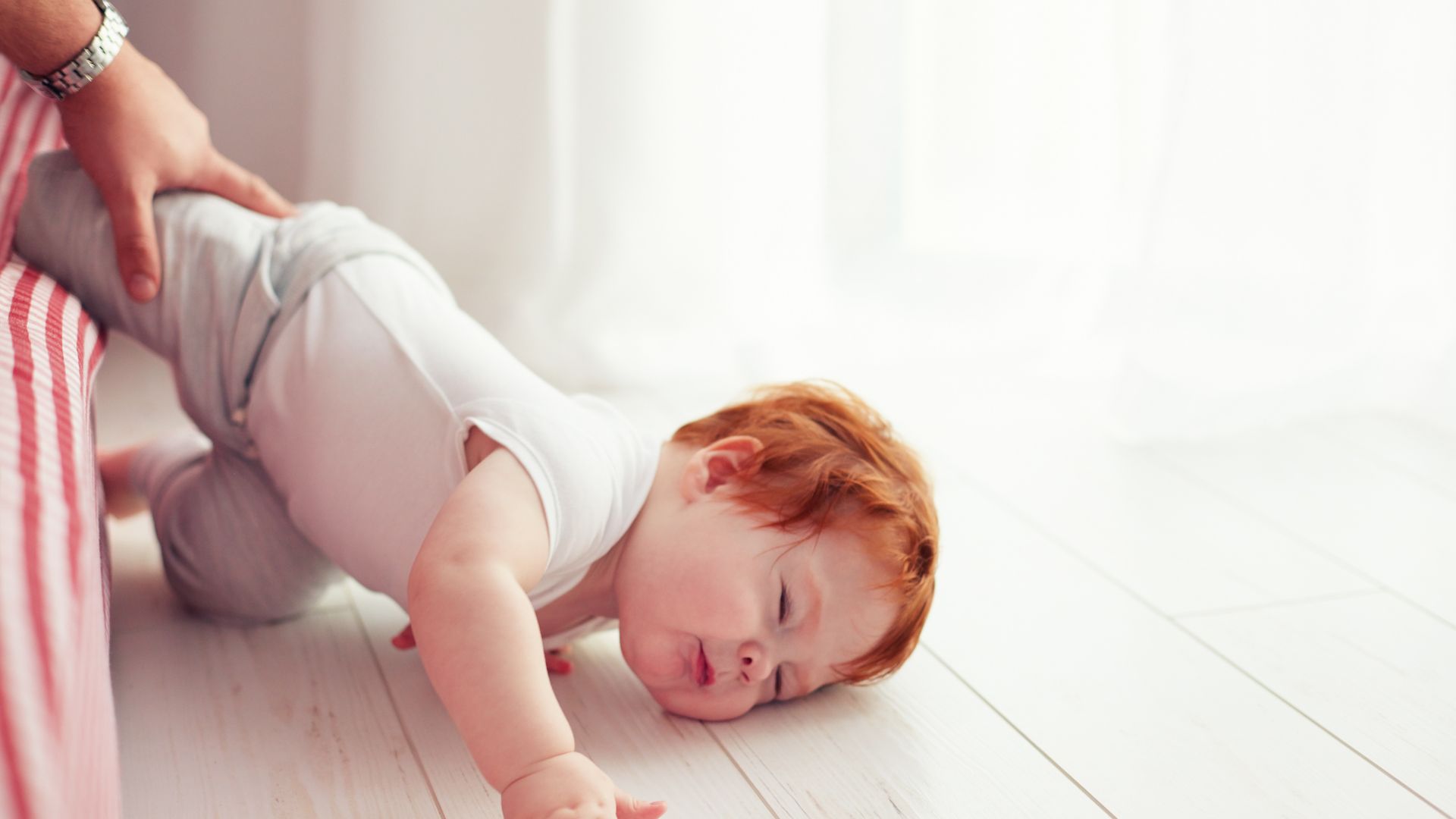 A hand reaches out to a baby who has fallen off the bed and hit their head