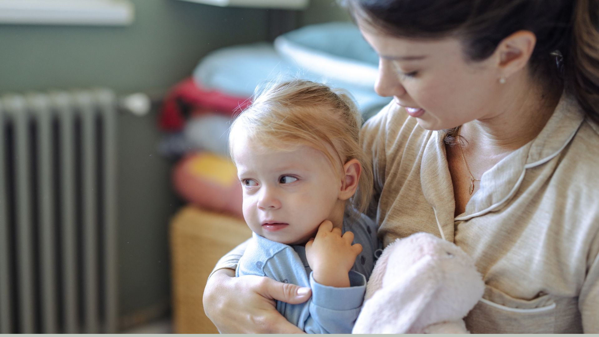 A mom comforting a toddler girl in her bedroom with a stuffed animal