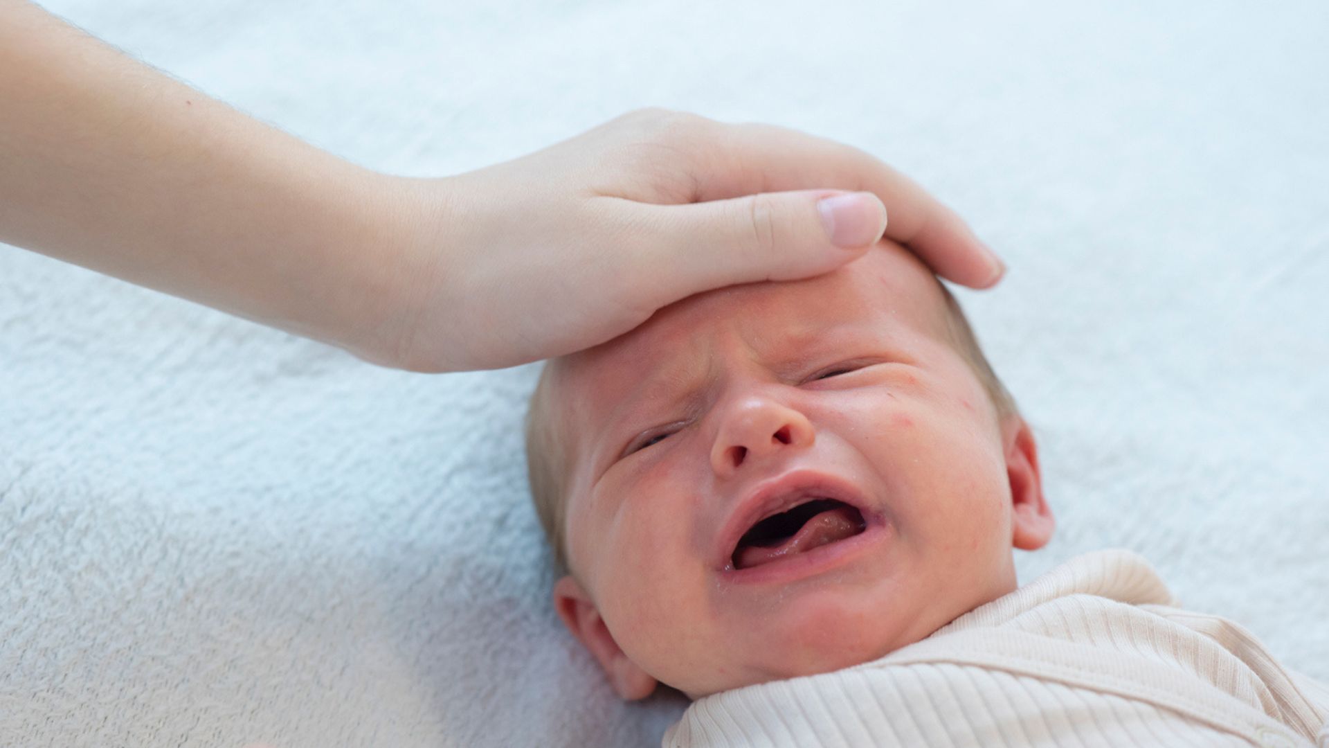A mom's hand stroking a crying baby's head