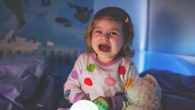 A toddler girl crying in bed in PJs after having a nightmare