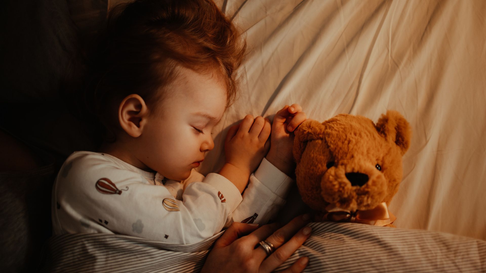 A toddler girl sleeping in her bed with a teddy bear beside her