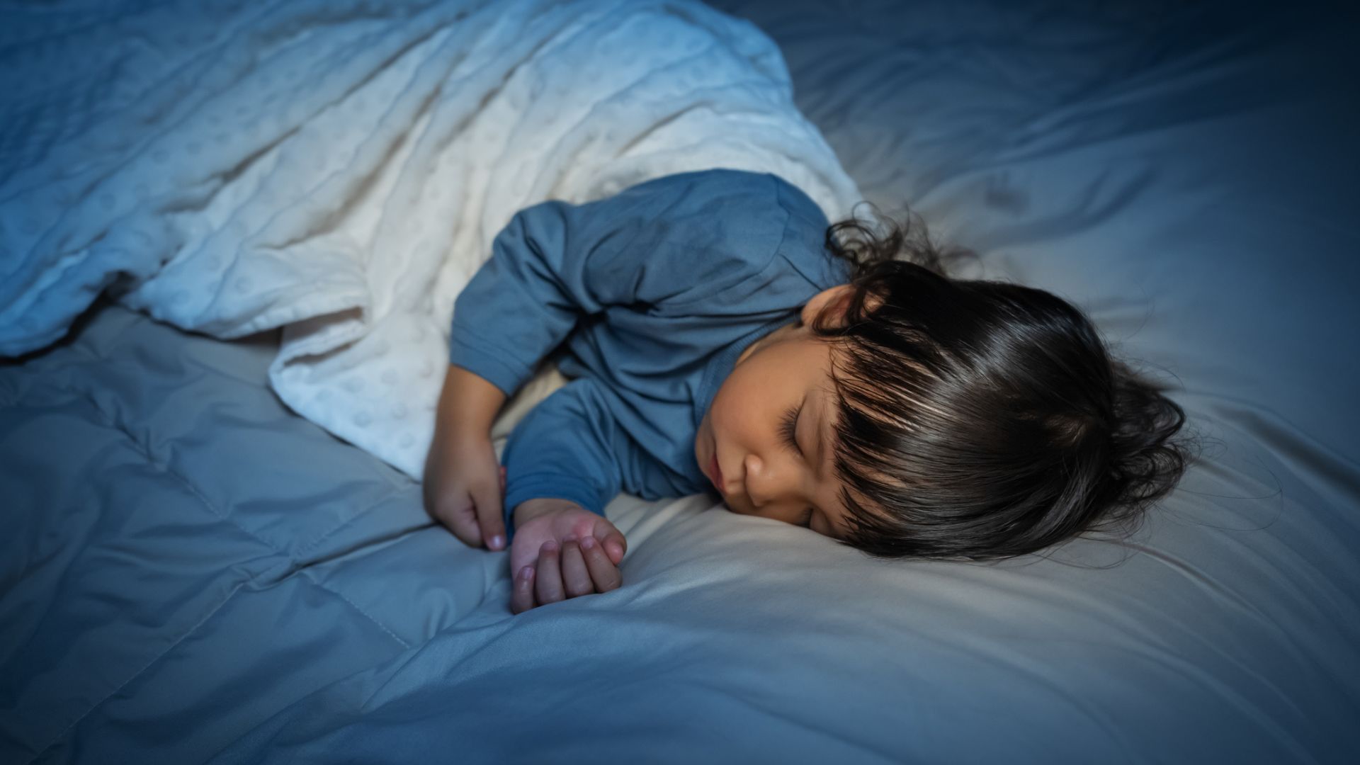 A toddler sleeping in bed at night covered with a blanket