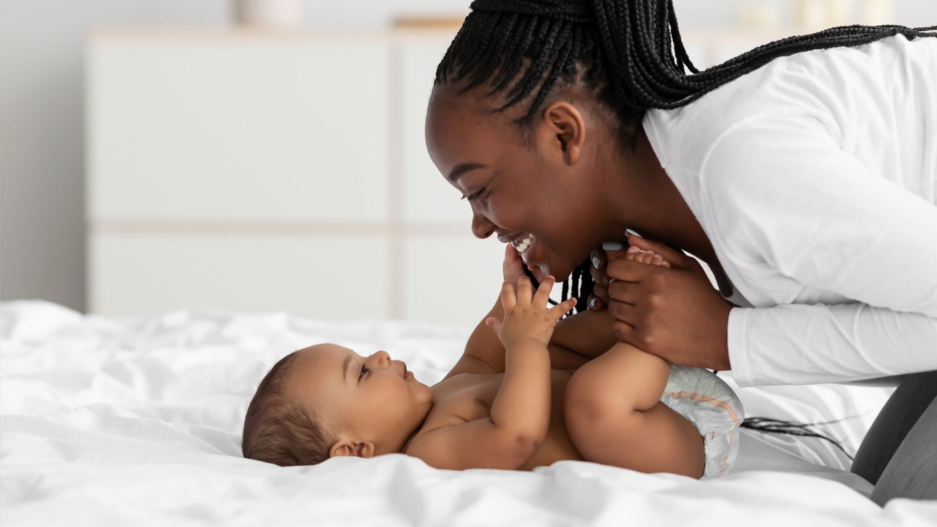 An African American mom playing with her baby on the bed