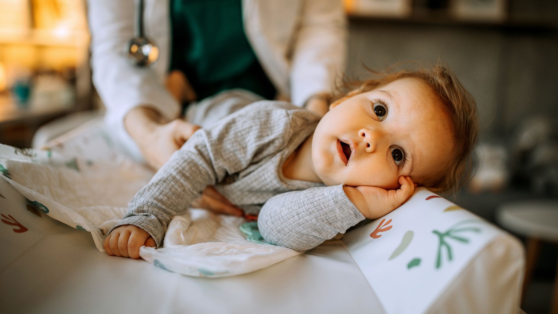 An older baby girl being held on a changing table by their parent