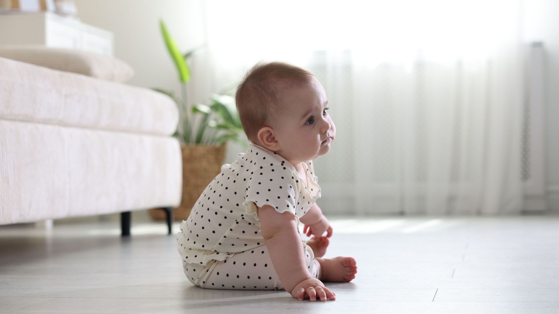 Baby in a polka dot outfit sitting on the floor in front of a sofa