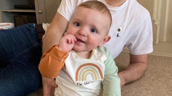 Finley Baker sits on the floor in a rainbow shirt.