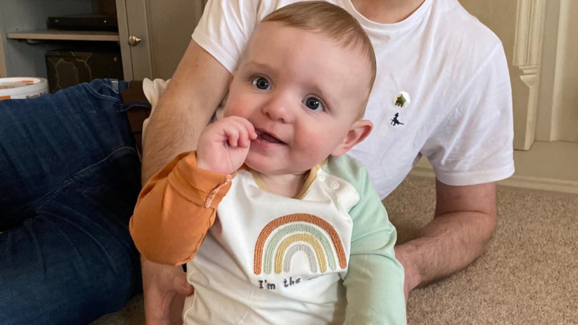 Finley Baker sits on the floor in a rainbow shirt.