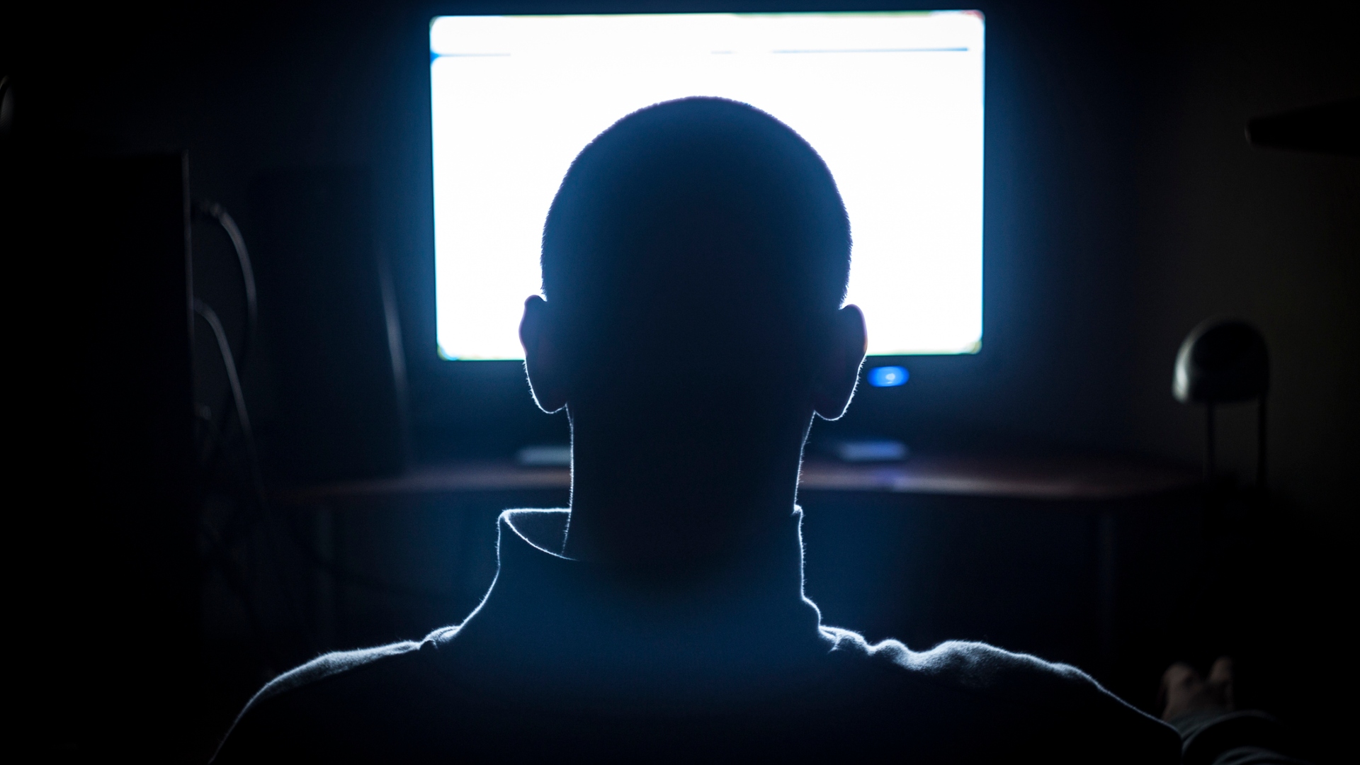 A man sits in a dark room in front of a bright screen