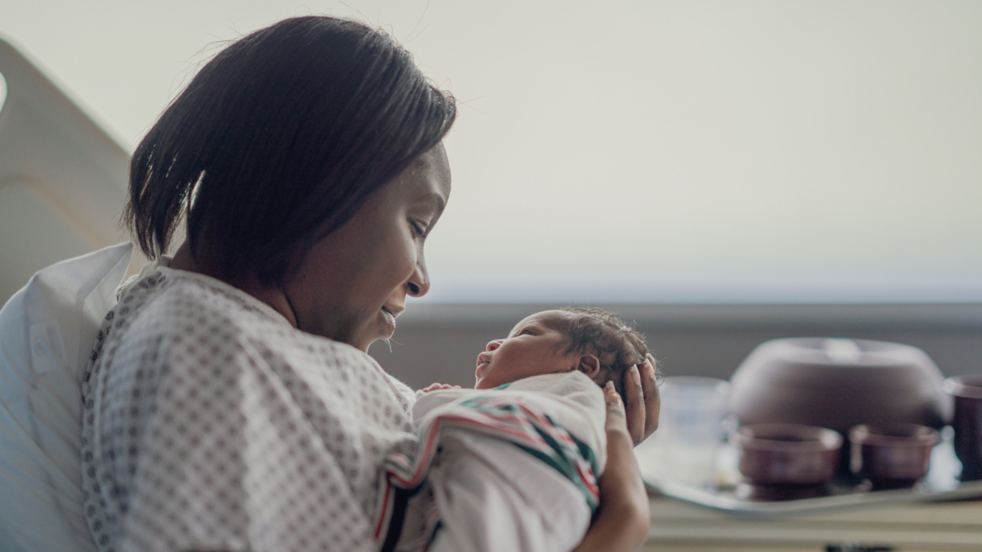 Black mom laying in her hospital bed looking down at the newborn in her arms