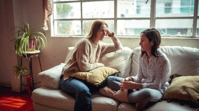 mom and tween daughter sitting on couch talking in front of window in living room