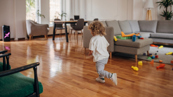toddler with curly hair in a white shirt and striped pants running in a living room