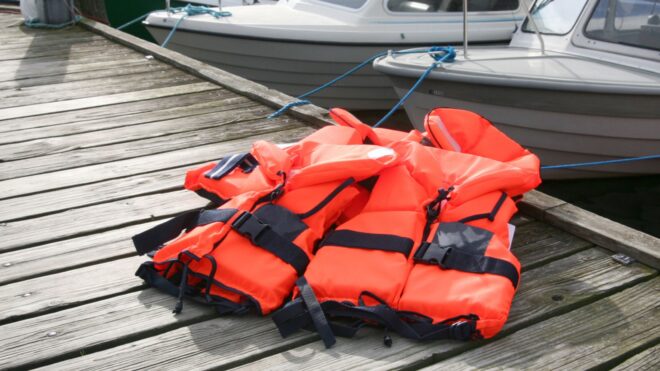 A couple orange life jackets on a dock near a boat
