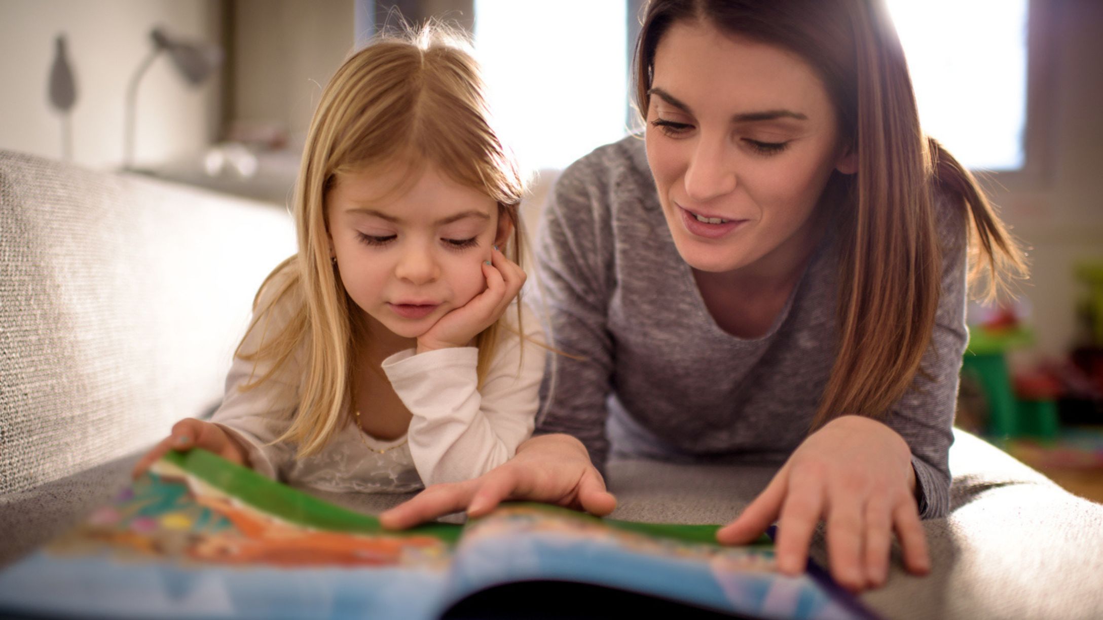 A mother and daughter reading a storybook together on their stomachs