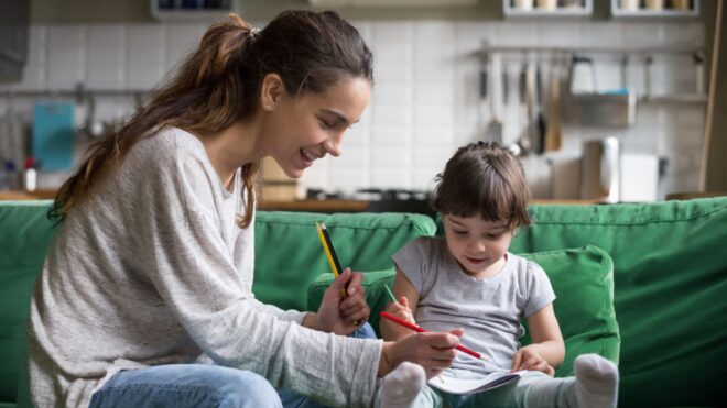 A young adult woman and a child coloring while sitting on a sofa