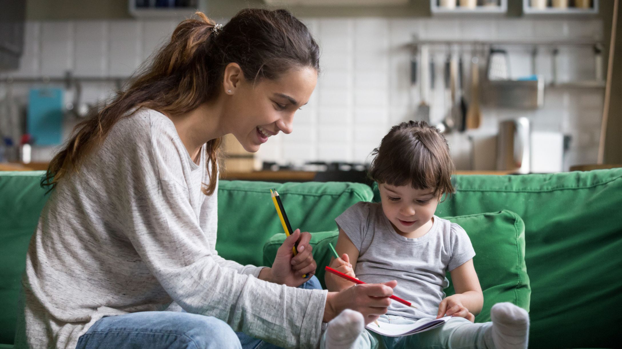 A young adult woman and a child coloring while sitting on a sofa
