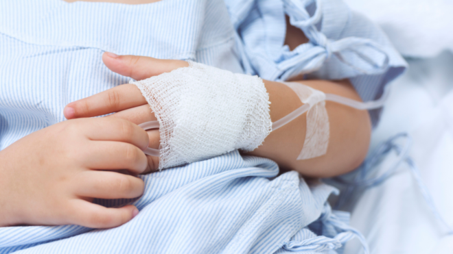 a young child in a hospital bed wearing a hospital gown with a bandaged hand
