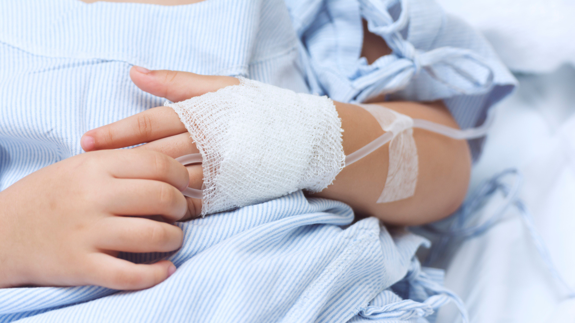 a young child in a hospital bed wearing a hospital gown with a bandaged hand