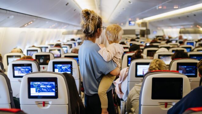 A mom carrying her toddler in between seats on an airplane
