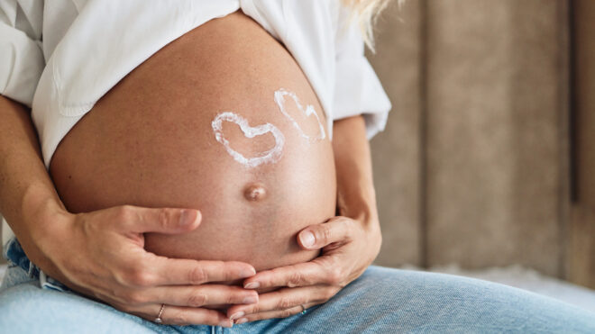 Pregnant woman embracing her belly. 2 Heart shapes on belly.