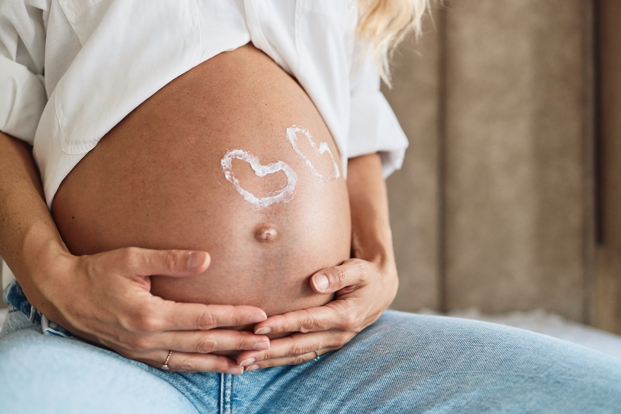 Pregnant woman embracing her belly. 2 Heart shapes on belly.